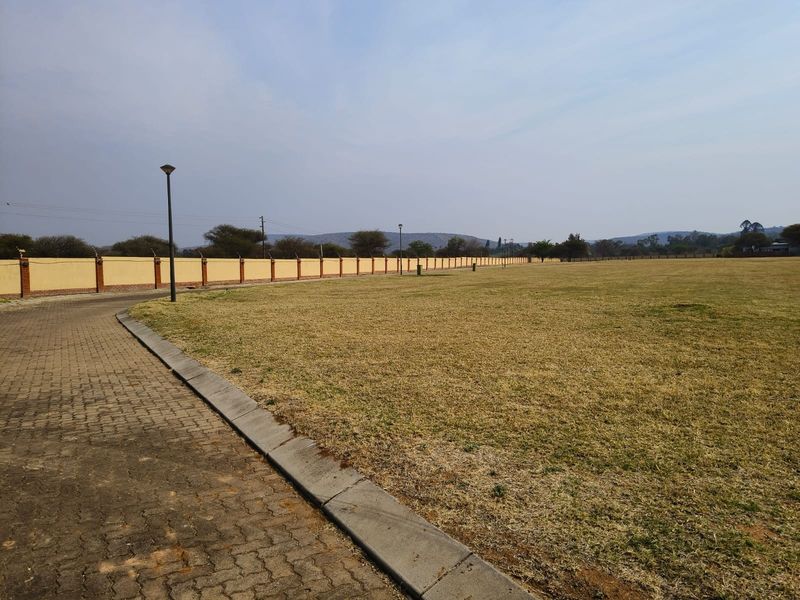 A spacious, level residential plot featuring a paved driveway, perimeter wall with electric fencing, and established grass area.