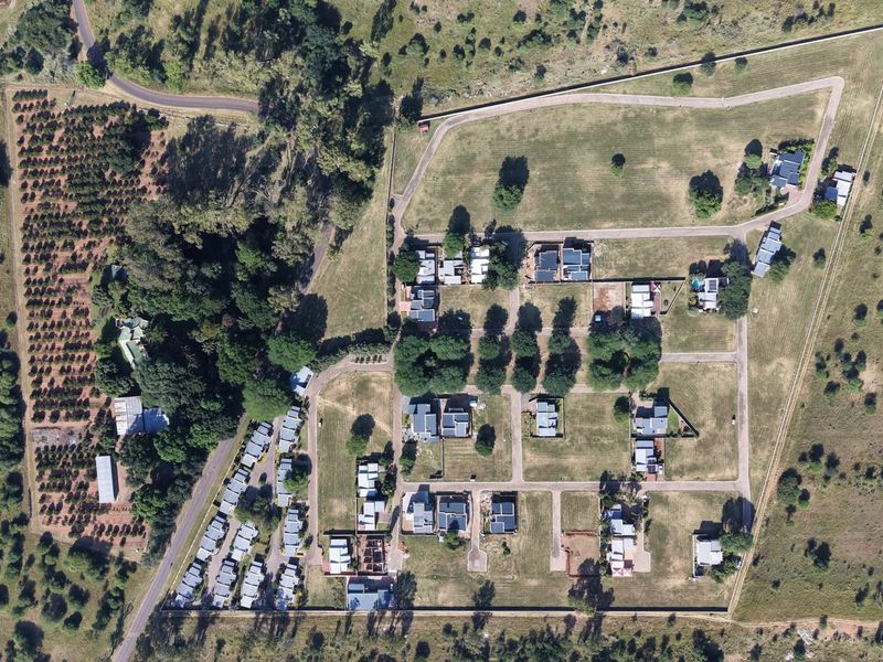 An aerial view of a residential estate development featuring paved internal roads, established landscaping, and multiple residential plots.