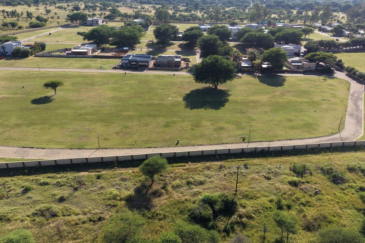 Aerial view of a large, level residential vacant land plot featuring established trees, boundary walling, and direct access to a paved road.