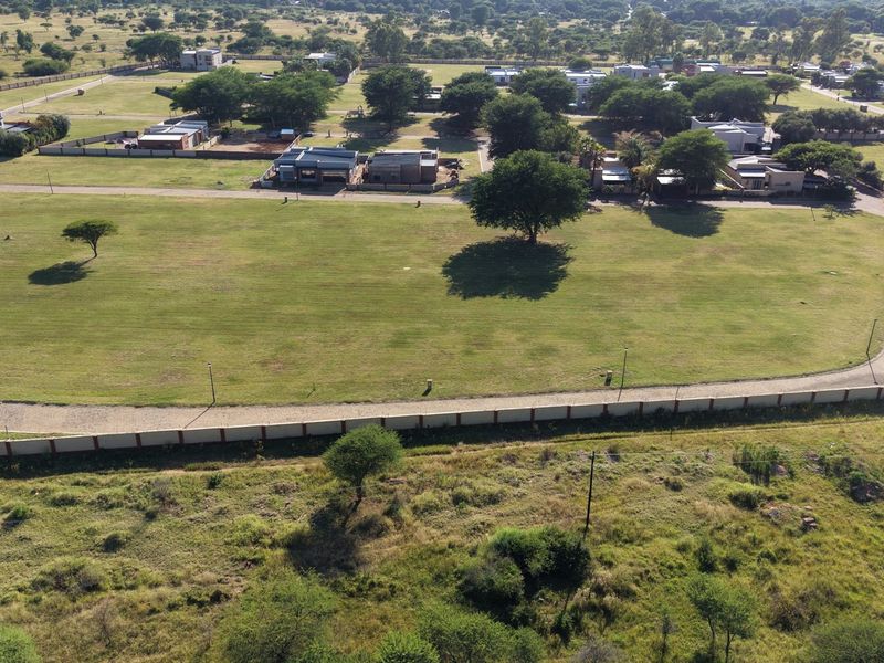 Aerial view of a large, level residential vacant land plot featuring established trees, boundary walling, and direct access to a paved road.