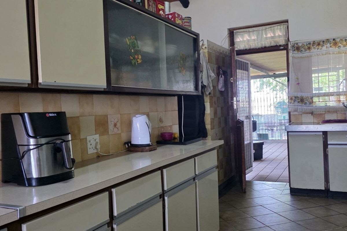 A dated kitchen featuring original cabinetry, tiled backsplash, and tiled flooring, with direct access to an outdoor patio area.