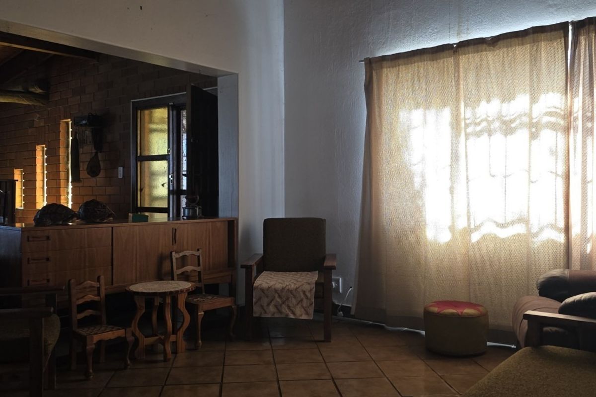 A living room area featuring tiled flooring and an exposed brick wall, with natural light entering through a large window.