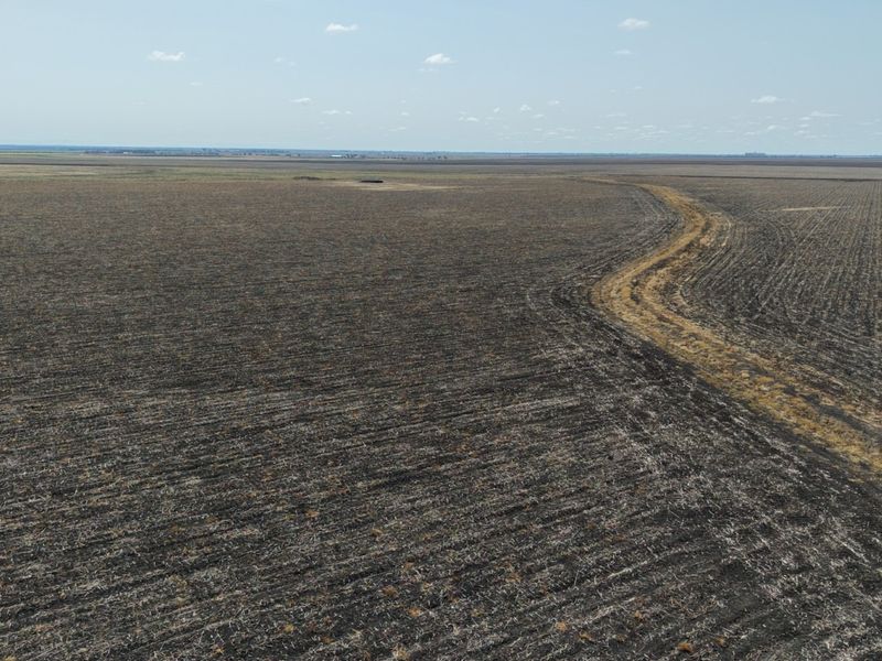 An aerial view of expansive, flat agricultural farmland featuring a dirt access track running through the cultivated fields.