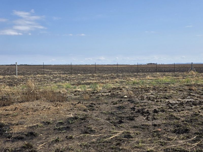 Expansive view of open farmland featuring cleared soil and perimeter wire fencing under a clear blue sky.