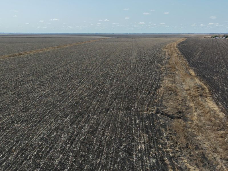 An aerial view of expansive, tilled agricultural farmland featuring a drainage or irrigation channel running through the property.