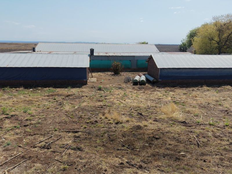 Aerial view of agricultural farm buildings featuring corrugated metal roofing and brick masonry construction set on a large rural plot.