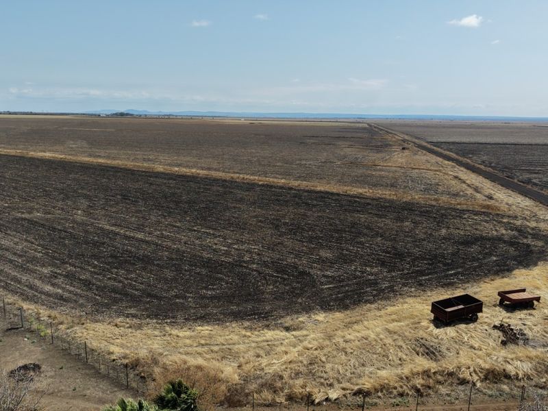 An aerial view of expansive agricultural farmland featuring tilled soil, open fields, and perimeter fencing.