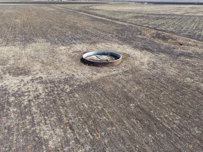 Aerial view of a large, circular concrete water reservoir situated in the middle of an expansive, dry agricultural field.
