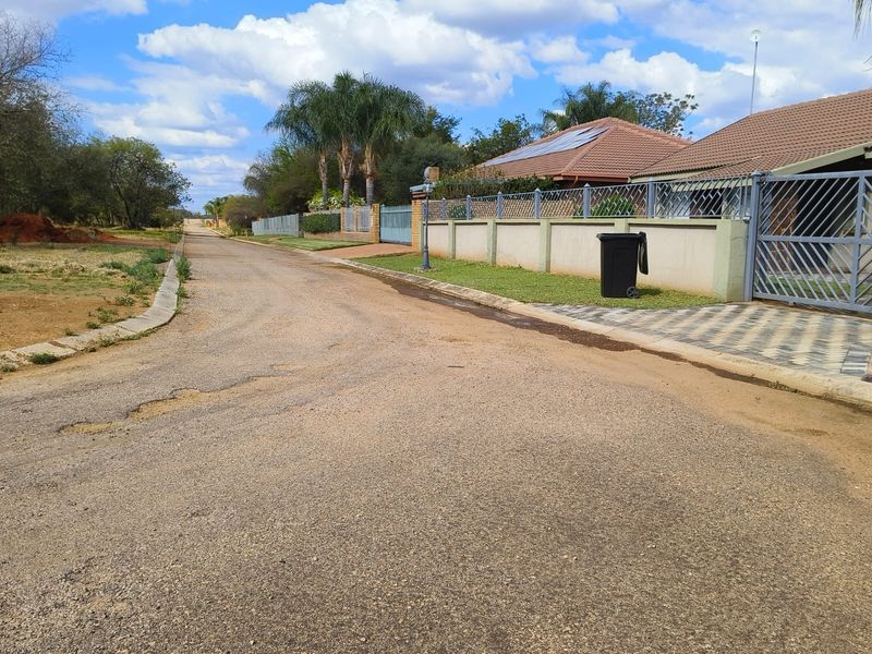 A street view showing the residential access road, perimeter fencing, and gated entrance to the property.