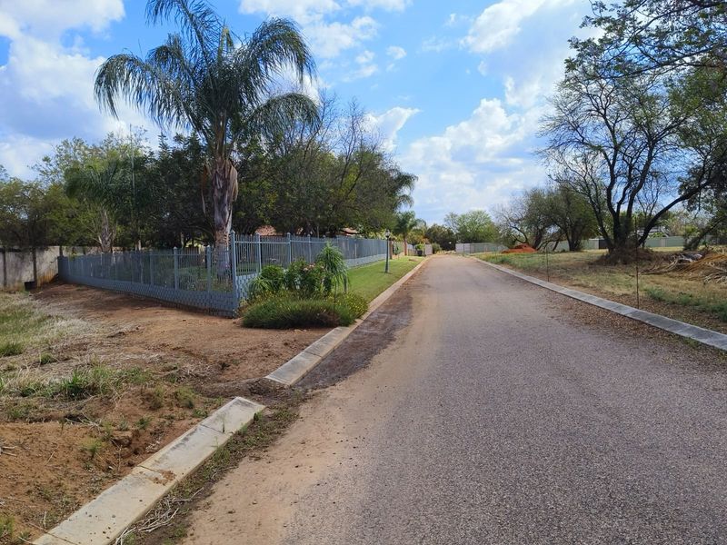A view of the residential street frontage featuring asphalt paving, concrete curbing, and established perimeter fencing with mature landscaping.