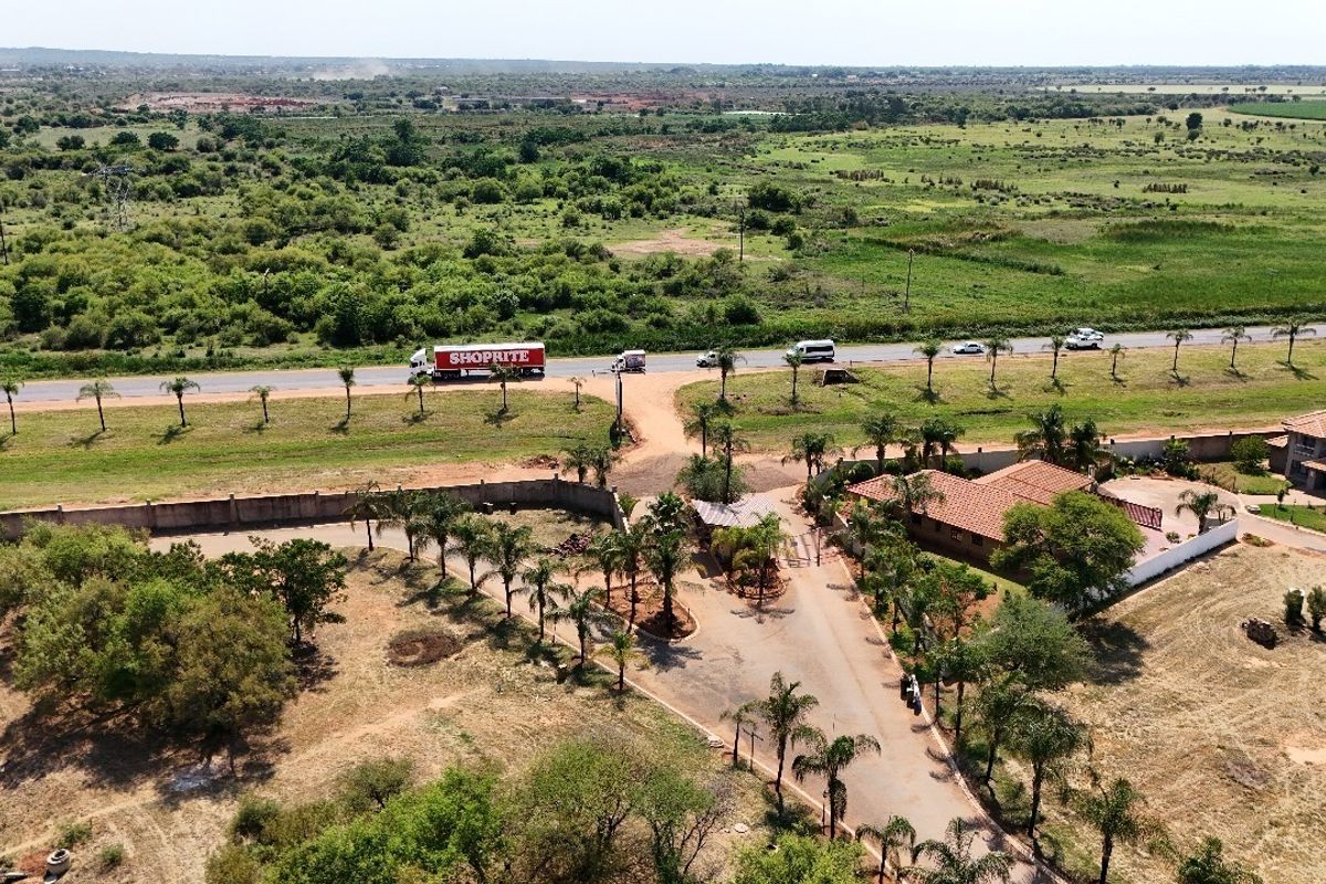 Aerial view of a residential property featuring a gated entrance, paved driveway, perimeter wall, and established palm tree landscaping.