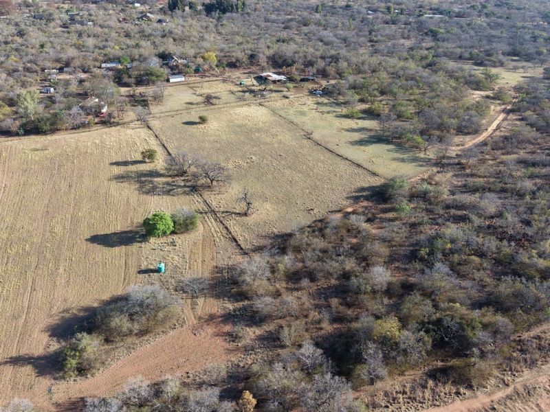 Aerial view of the small holding property featuring open fields, natural vegetation, perimeter fencing, and a water storage tank.