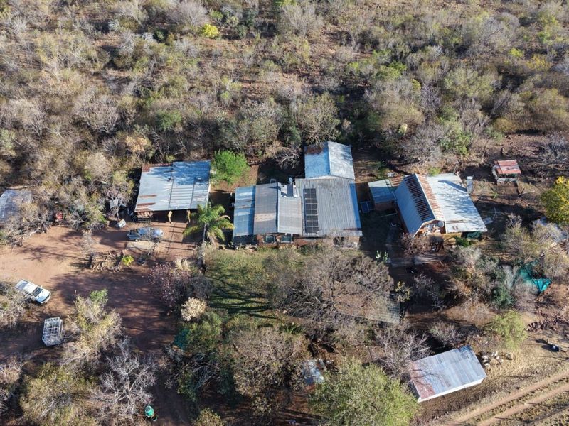 Aerial view of a small holding property featuring multiple outbuildings with corrugated metal roofs, solar panels, and surrounding natural bushveld vegetation.