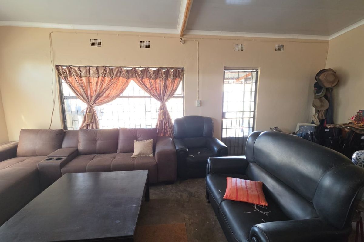 A living room area featuring security gates and burglar bars on windows, with visible electrical conduit and dated wall finishes.