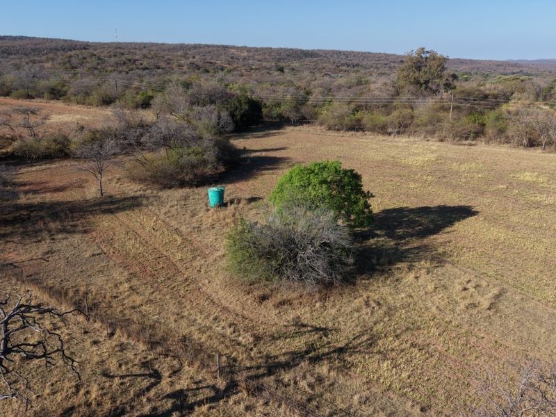 Aerial view of a large, open small holding plot featuring natural vegetation, dry grassland, and a standalone water storage tank.