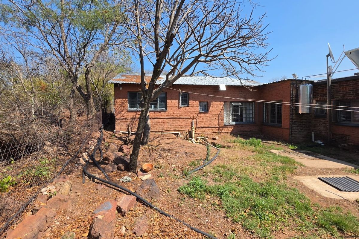 Rear view of a rustic brick small holding dwelling featuring a corrugated metal roof, steel windows, and an installed solar water heating system.