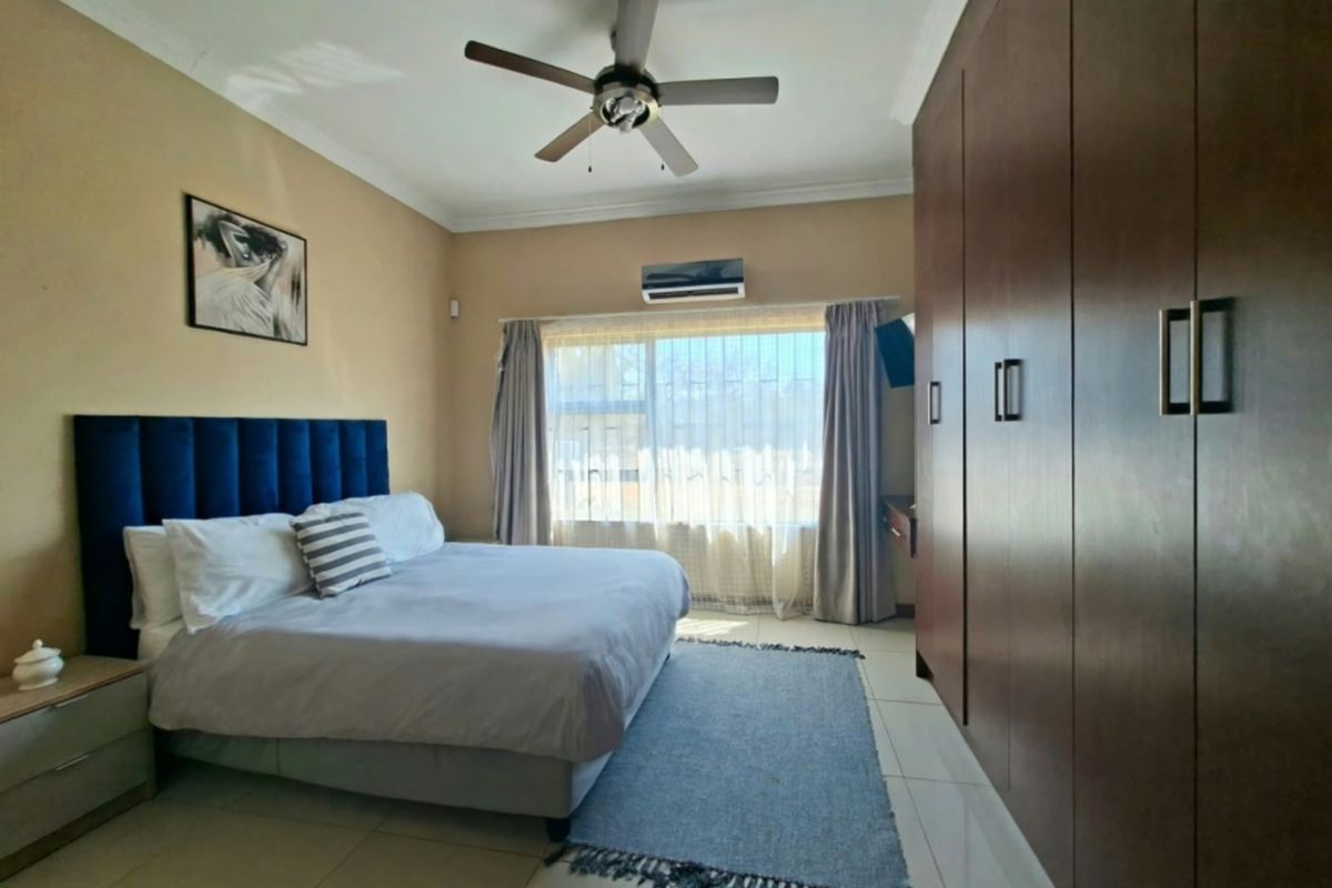 Spacious bedroom featuring built-in wooden cupboards, tiled flooring, a ceiling fan, and an integrated air conditioning unit.