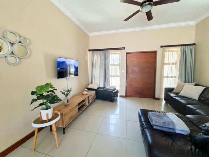 A bright living room featuring large windows, tiled flooring, and a ceiling fan, providing a comfortable and functional space.