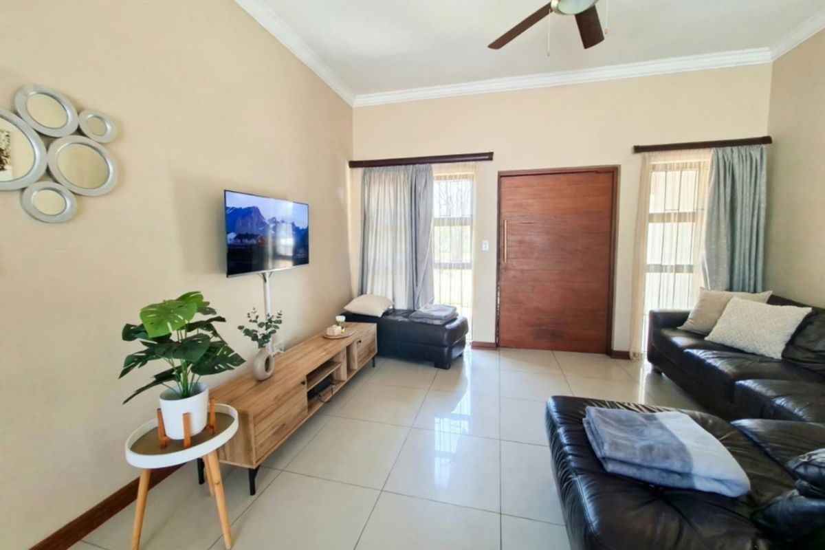 A bright living room featuring large windows, tiled flooring, and a ceiling fan, providing a comfortable and functional space.