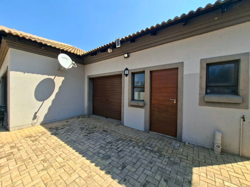 A paved rear courtyard area featuring a roller garage door, a timber entrance door, and exterior lighting under a tiled roof overhang.
