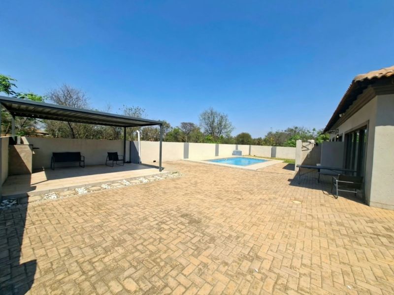 Spacious rear courtyard featuring a paved patio area, a covered outdoor entertainment space, and a private swimming pool.