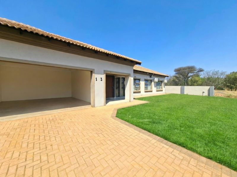 Front exterior view of the house featuring a paved driveway, integrated carport, well-maintained lawn, and boundary wall.