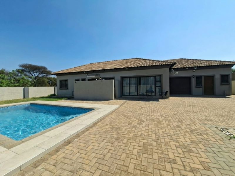 Rear exterior view of the house featuring a swimming pool, extensive paved patio area, and direct access to the living space via sliding doors.