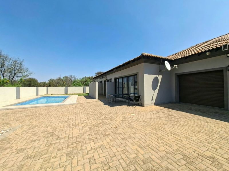 Rear exterior view featuring a paved patio area, a swimming pool, and access to the garage and main living space via sliding doors.