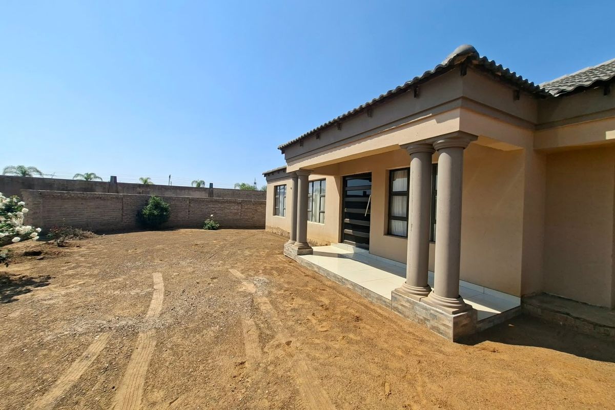 Rear view of the house featuring a covered patio with concrete columns and a large, unlandscaped yard enclosed by a perimeter wall.