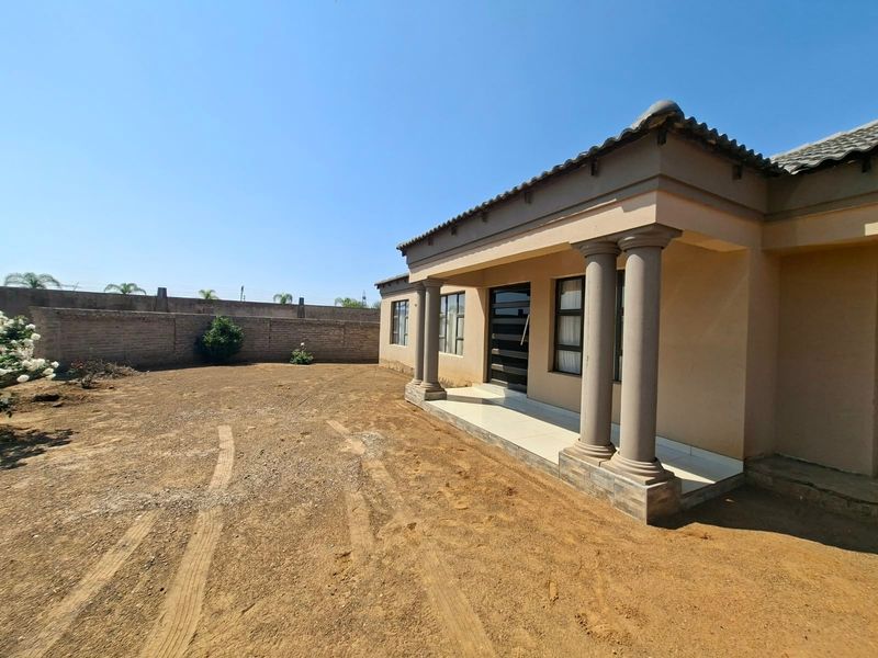 Rear view of the house featuring a covered patio with concrete columns and a large, unlandscaped yard enclosed by a perimeter wall.