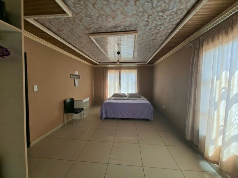 Spacious bedroom featuring large format floor tiles and a decorative tray ceiling with integrated lighting.