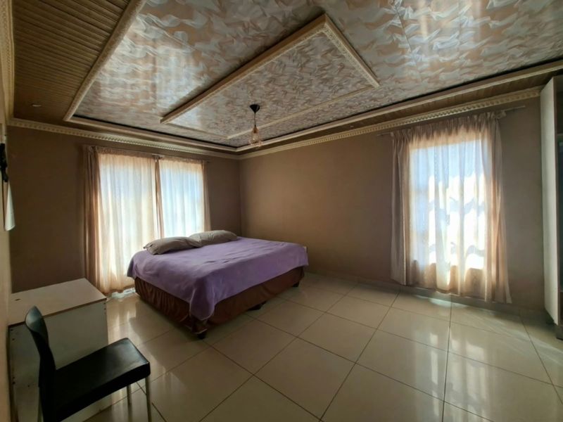 Spacious bedroom featuring large format floor tiles, decorative ceiling panels with integrated molding, and dual windows providing ample natural light.