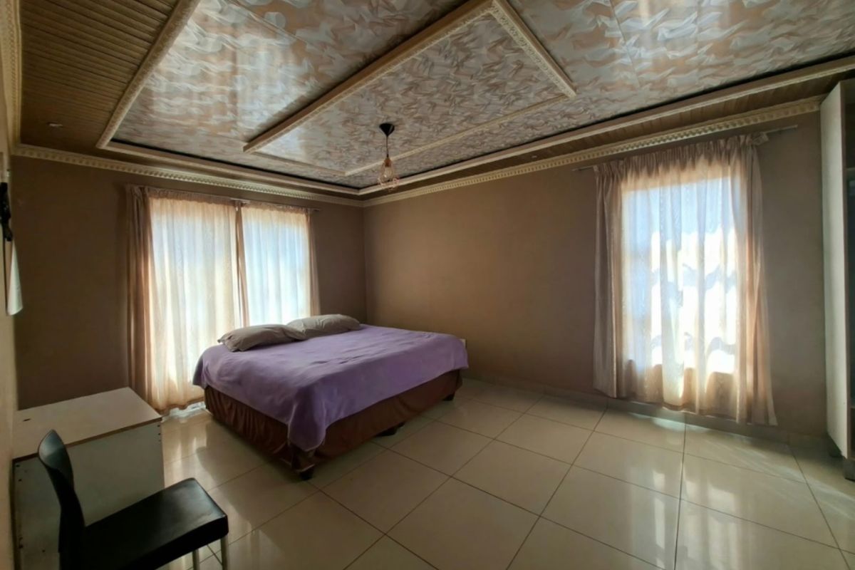 Spacious bedroom featuring large format floor tiles, decorative ceiling panels with integrated molding, and dual windows providing ample natural light.