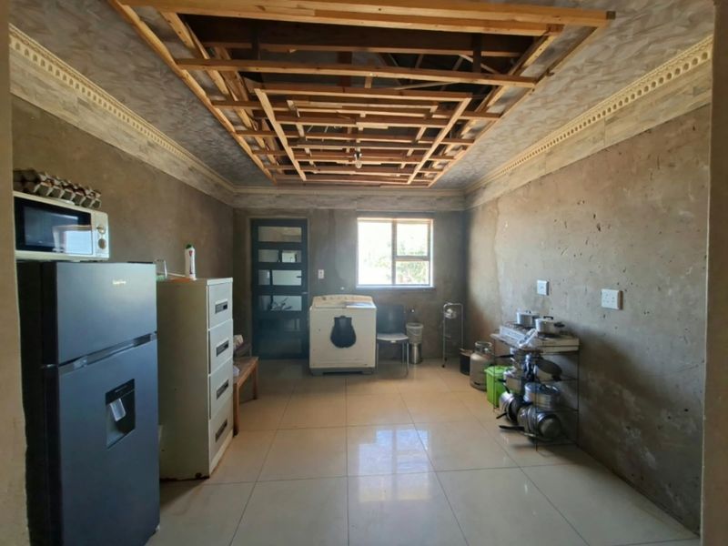 A kitchen area currently under renovation, featuring tiled floors, exposed ceiling joists, and unfinished wall surfaces awaiting final finishes.