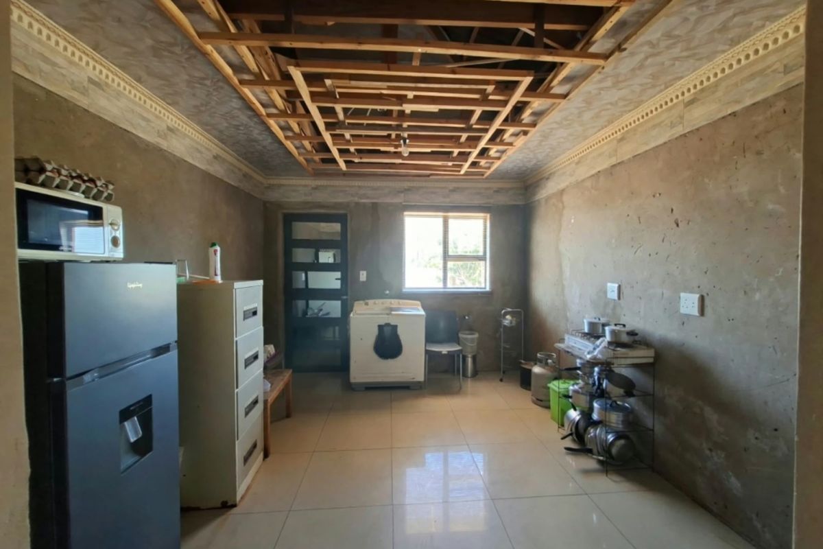 A kitchen area currently under renovation, featuring tiled floors, exposed ceiling joists, and unfinished wall surfaces awaiting final finishes.