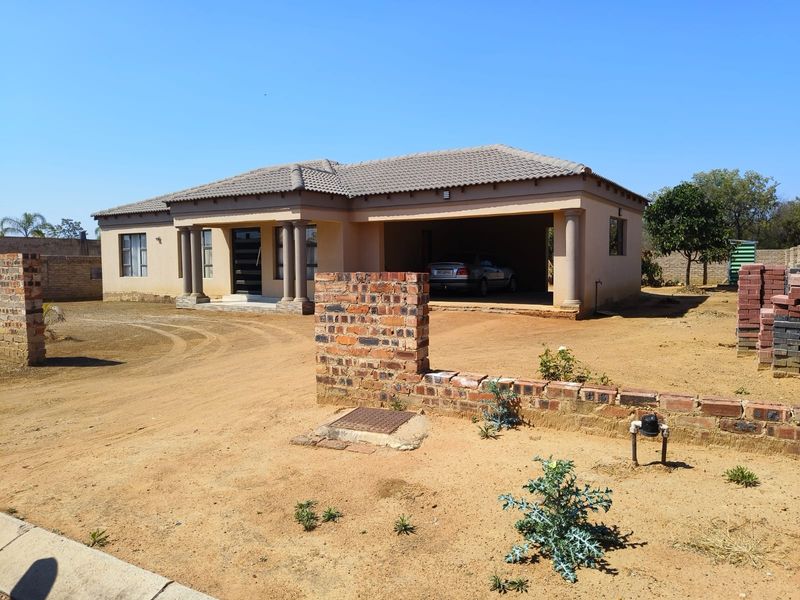Single-story residential house featuring a tiled roof, covered garage, and decorative columns, set on a large, unlandscaped plot with a brick boundary wall.