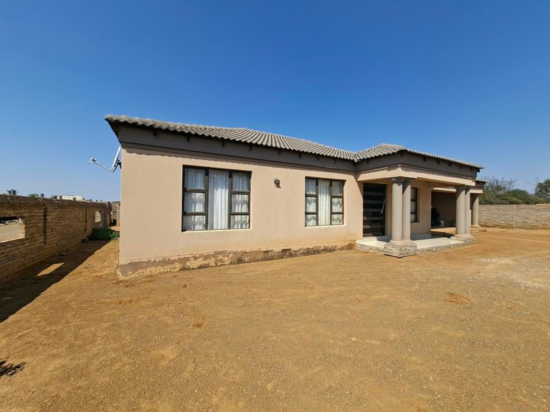 Single-story residential home featuring a tiled roof, covered entrance porch with concrete columns, and aluminium window frames, set on an unlandscaped dirt plot.