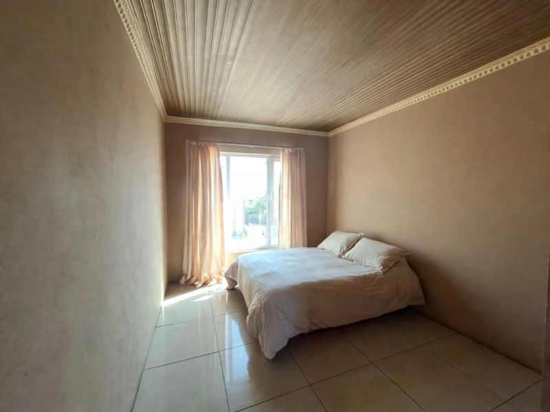 A bedroom featuring tiled flooring and a distinctive timber panelled ceiling with decorative cornice detailing.