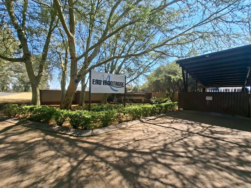 Entrance view of the Eau Montagne residential estate featuring a paved driveway, security gate, and established garden landscaping.