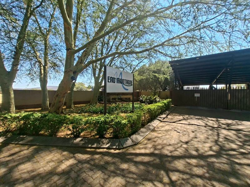 Entrance view of the property featuring a paved driveway, security gate, and established landscaping with mature trees and signage.