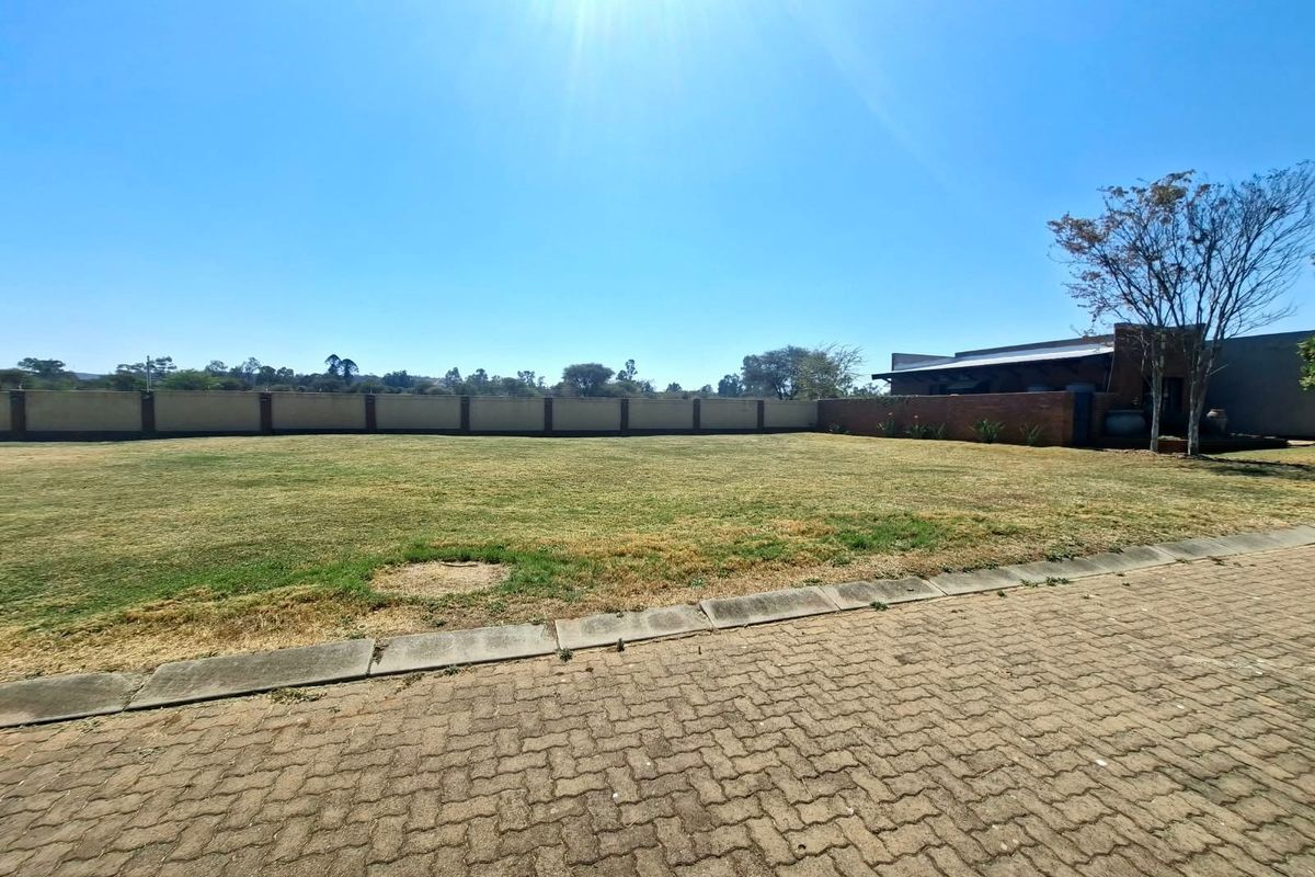 A spacious, level residential plot featuring a well-defined perimeter brick wall, established lawn, and paved driveway access.