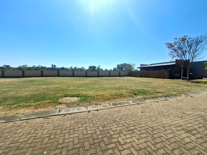 A spacious, level residential plot featuring a well-defined perimeter brick wall, established lawn, and paved driveway access.