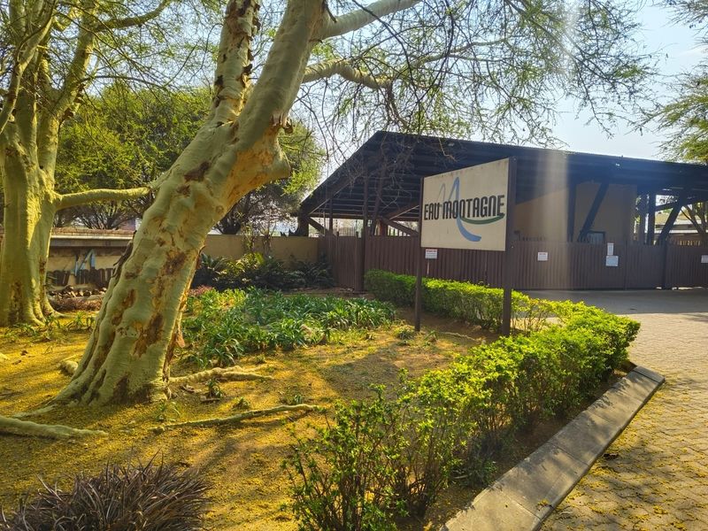 Entrance view of the Eau Montagne property featuring a paved driveway, landscaped garden area, and secure gated access.
