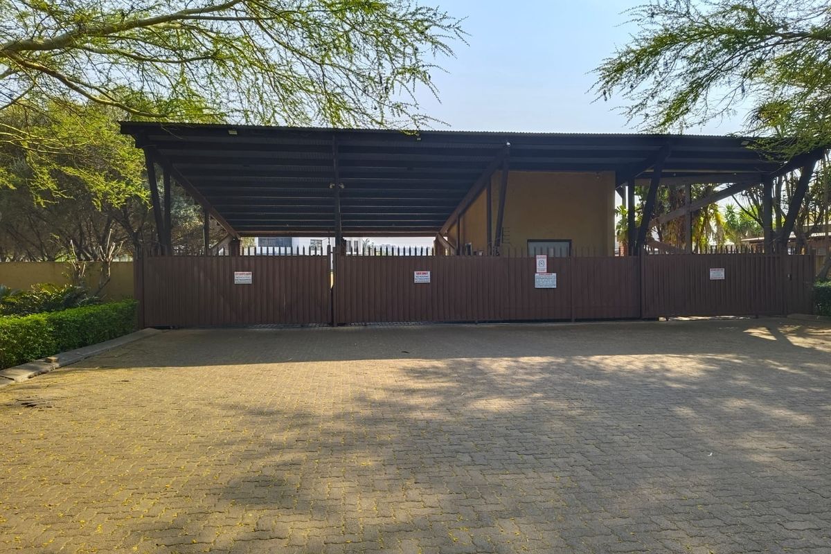 Front view of the property featuring a paved driveway, secure metal gate, and a large covered carport structure.