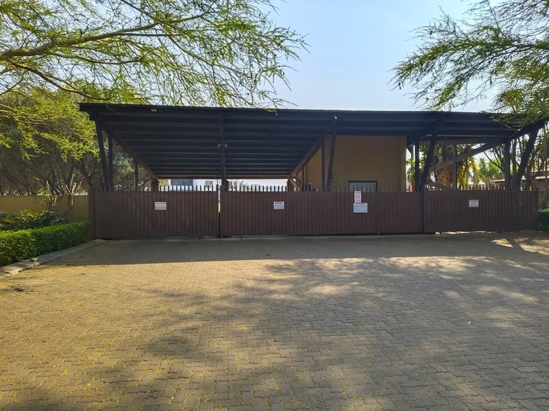 Front view of the property featuring a paved driveway, secure metal gate, and a large covered carport structure.