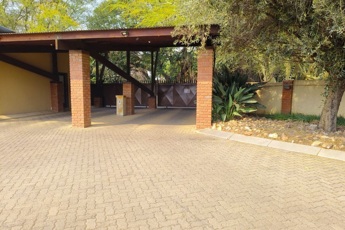 A well-maintained entrance area featuring a paved driveway, brick pillars supporting a timber roof structure, and a secure automated gate.
