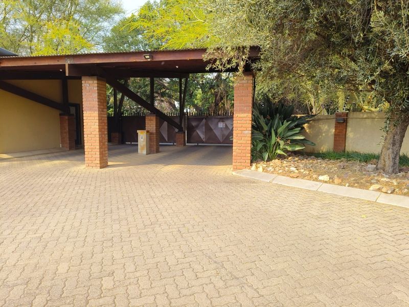 A well-maintained entrance area featuring a paved driveway, brick pillars supporting a timber roof structure, and a secure automated gate.