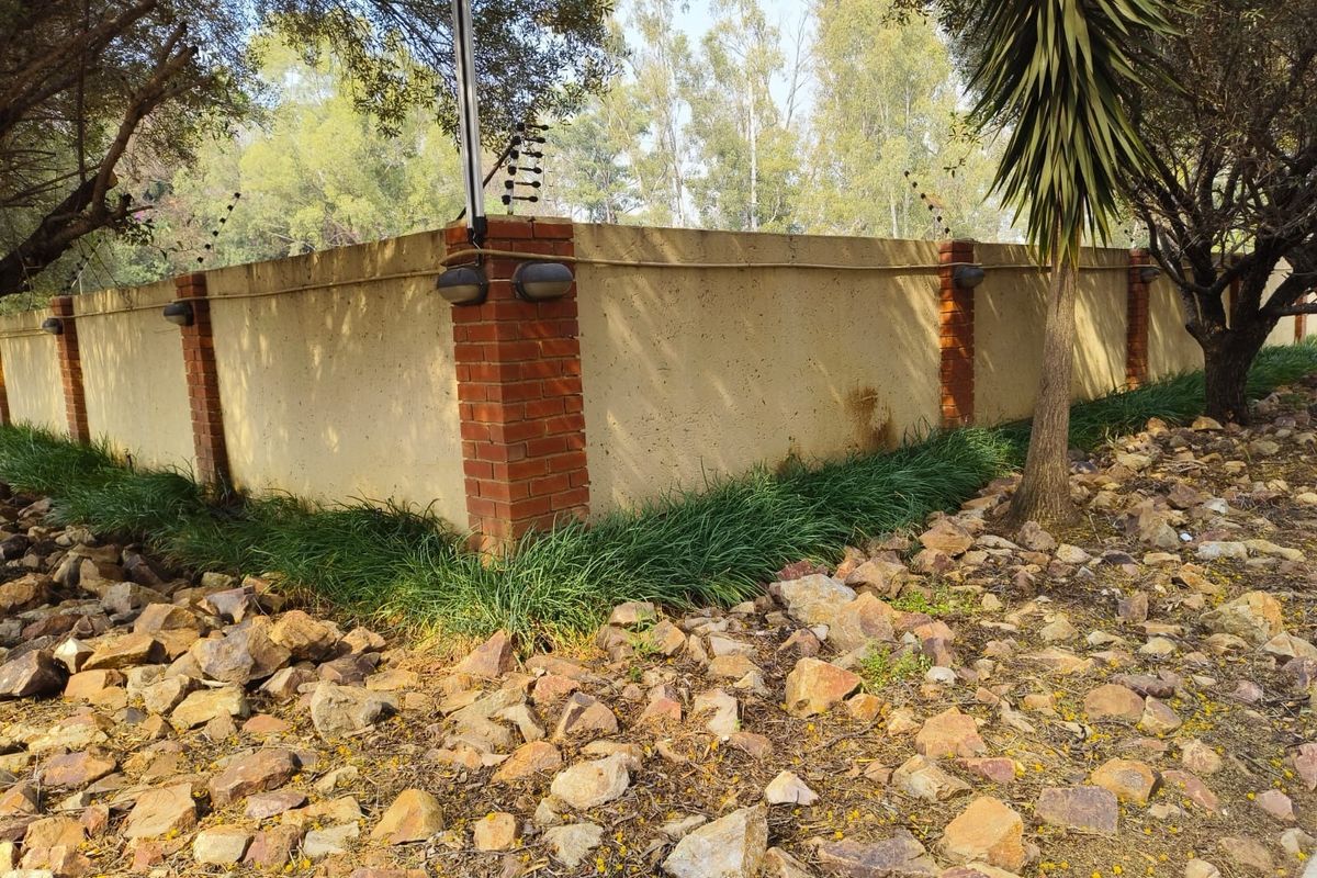 A view of the property's perimeter boundary wall featuring brick pillars, integrated exterior lighting, and security electric fencing.