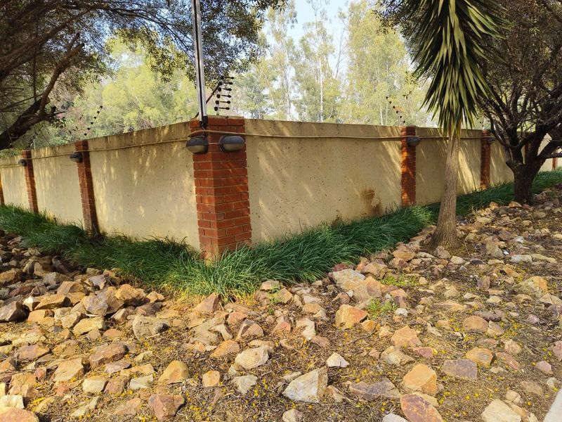 A view of the property's perimeter boundary wall featuring brick pillars, integrated exterior lighting, and security electric fencing.