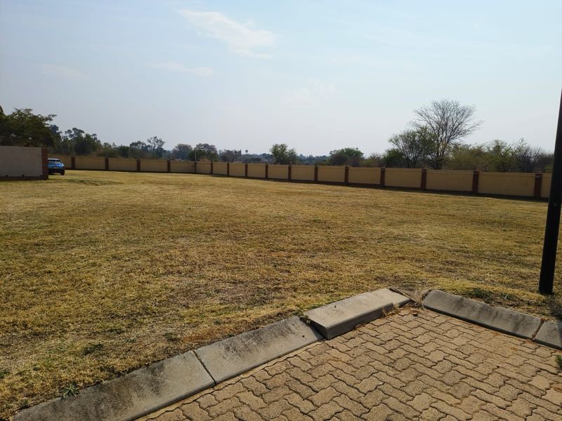 A spacious, level residential plot featuring a perimeter boundary wall and paved driveway access, offering a clear area for potential development.